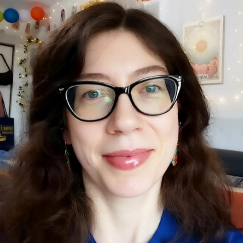 Kate LaDew Author Photo Kate LaDew, an author with glasses and long brown hair, smiles at the camera